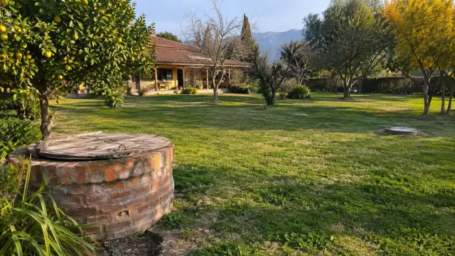 Noria de ladrillo en primer plano y, a lo lejos, la tapa de la cámara en el patio de una casa de campo con cerros