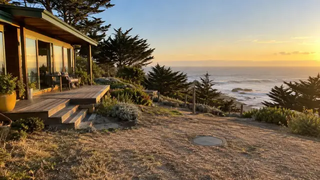 Casa de madera en una loma frente al mar de Pichilemu, con cipreses y la tapa de la cámara en el patio